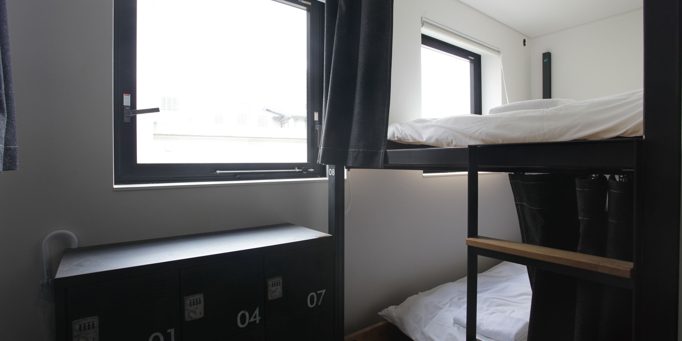 A dormitory-style room with bunk beds, a window, and a built-in desk with storage drawers.