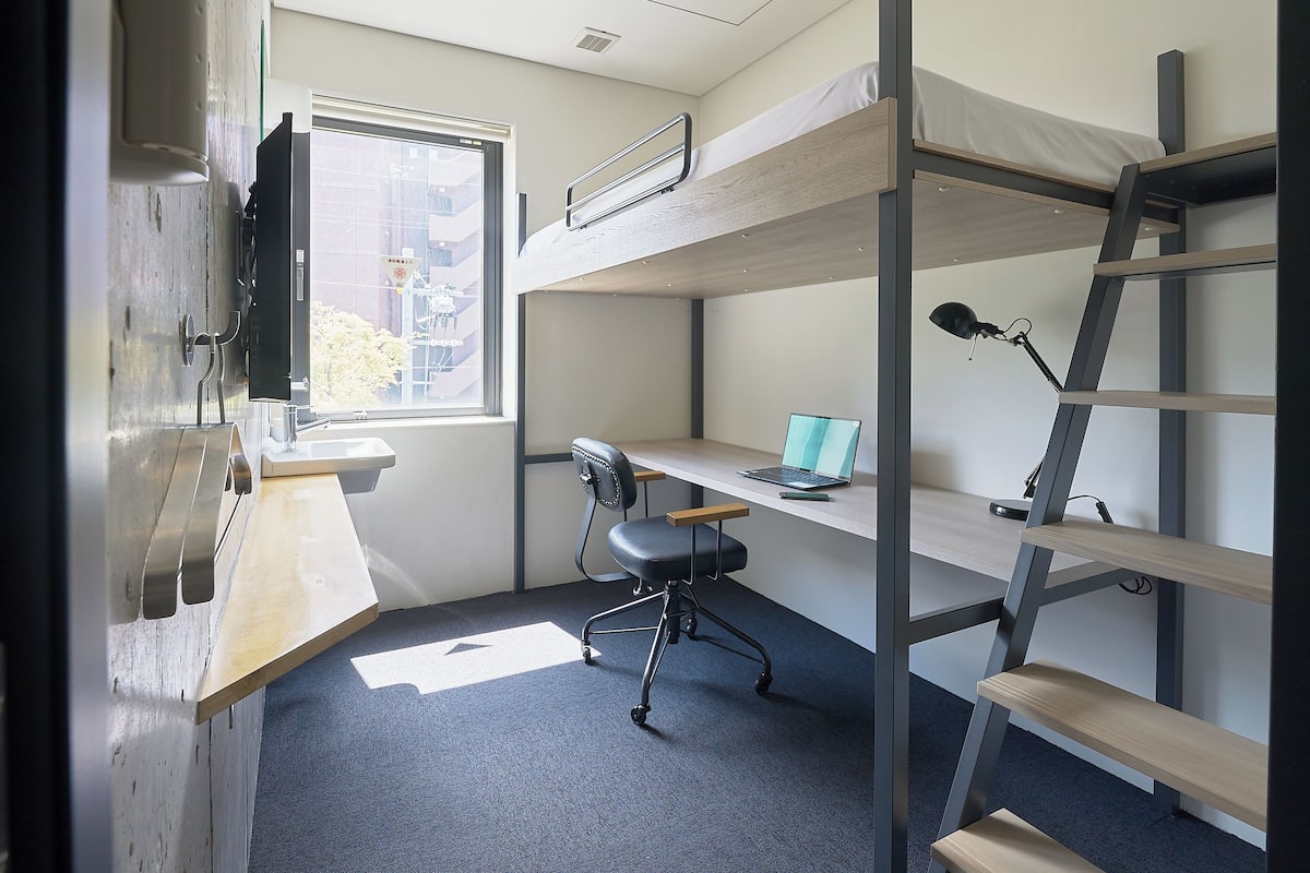 A bunk bed room with a desk, chair, and a window.