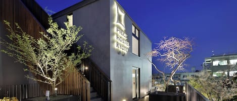 A modern building with a staircase, a sign reading 'PRESERVE HOSTEL KYOTO,' and two trees in front.