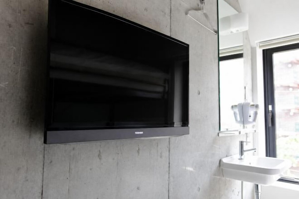 A modern bathroom with a mounted TV, a sink, and a window.