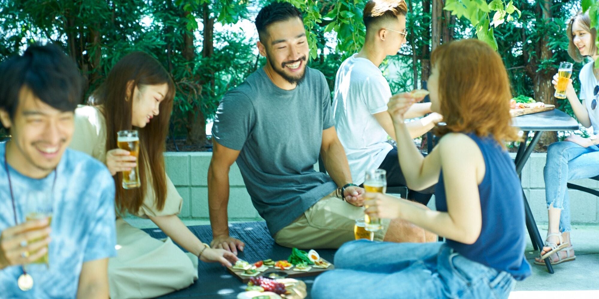 A group of people sitting on the ground outdoors, eating and drinking.