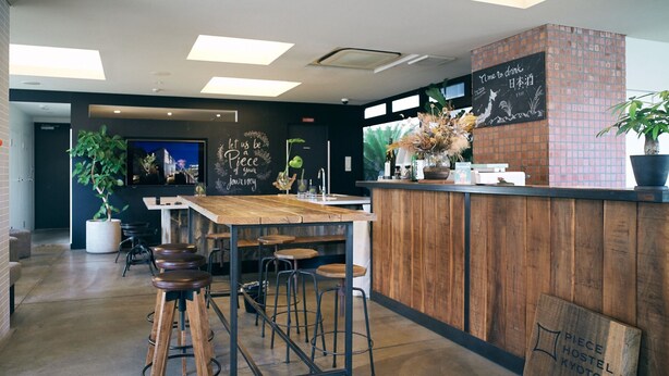 A modern cafe with a wooden counter, bar stools, and a chalkboard with motivational writing. - Piece Hostel Kyoto (Kyoto)
