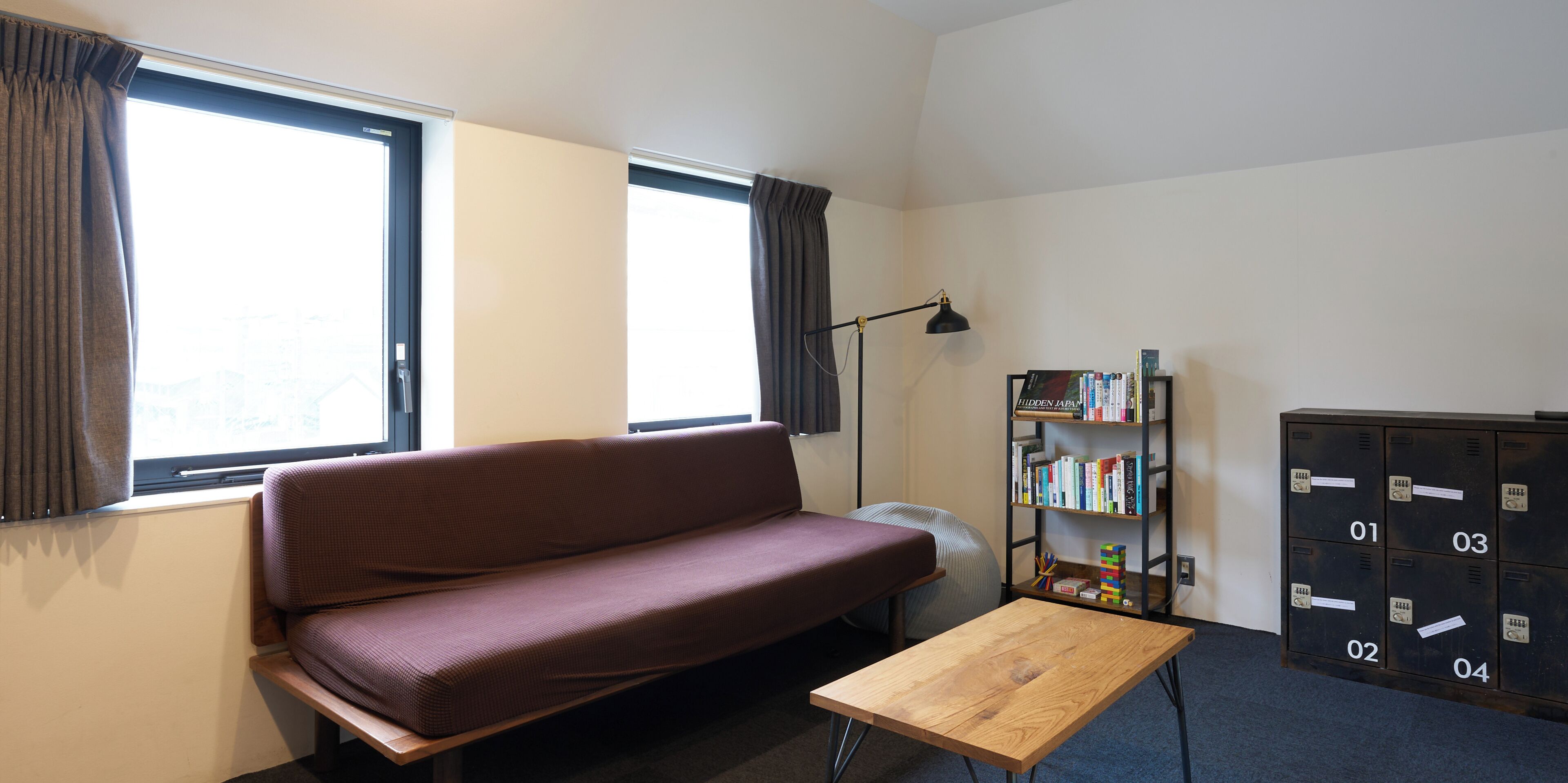 Une pièce comprenant un canapé, une petite table, une bibliothèque, un radiateur et une fenêtre avec des rideaux.