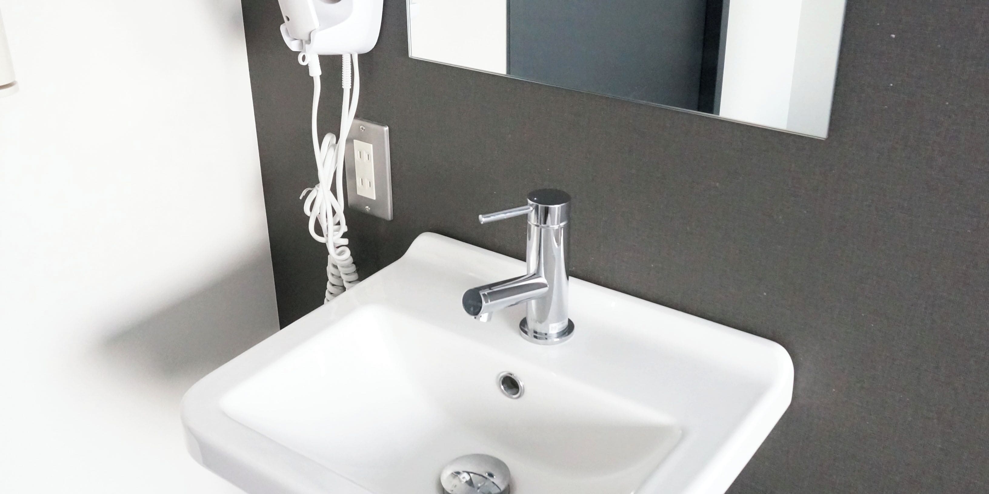 A white bathroom sink with a chrome faucet, a mirror above it, and a hairdryer plugged in on the wall.