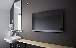 A modern bathroom with a flat-screen TV mounted on the wall, a white sink, and a mirror. - Piece Hostel Kyoto (Kyoto)