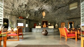 A lobby with a stone ceiling, wooden chairs, a reception desk, and a large vase. - Brys Caves (Salt)