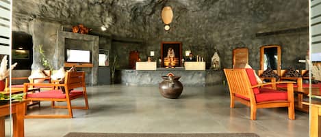 A lobby with a stone ceiling, wooden chairs, a reception desk, and a large vase.