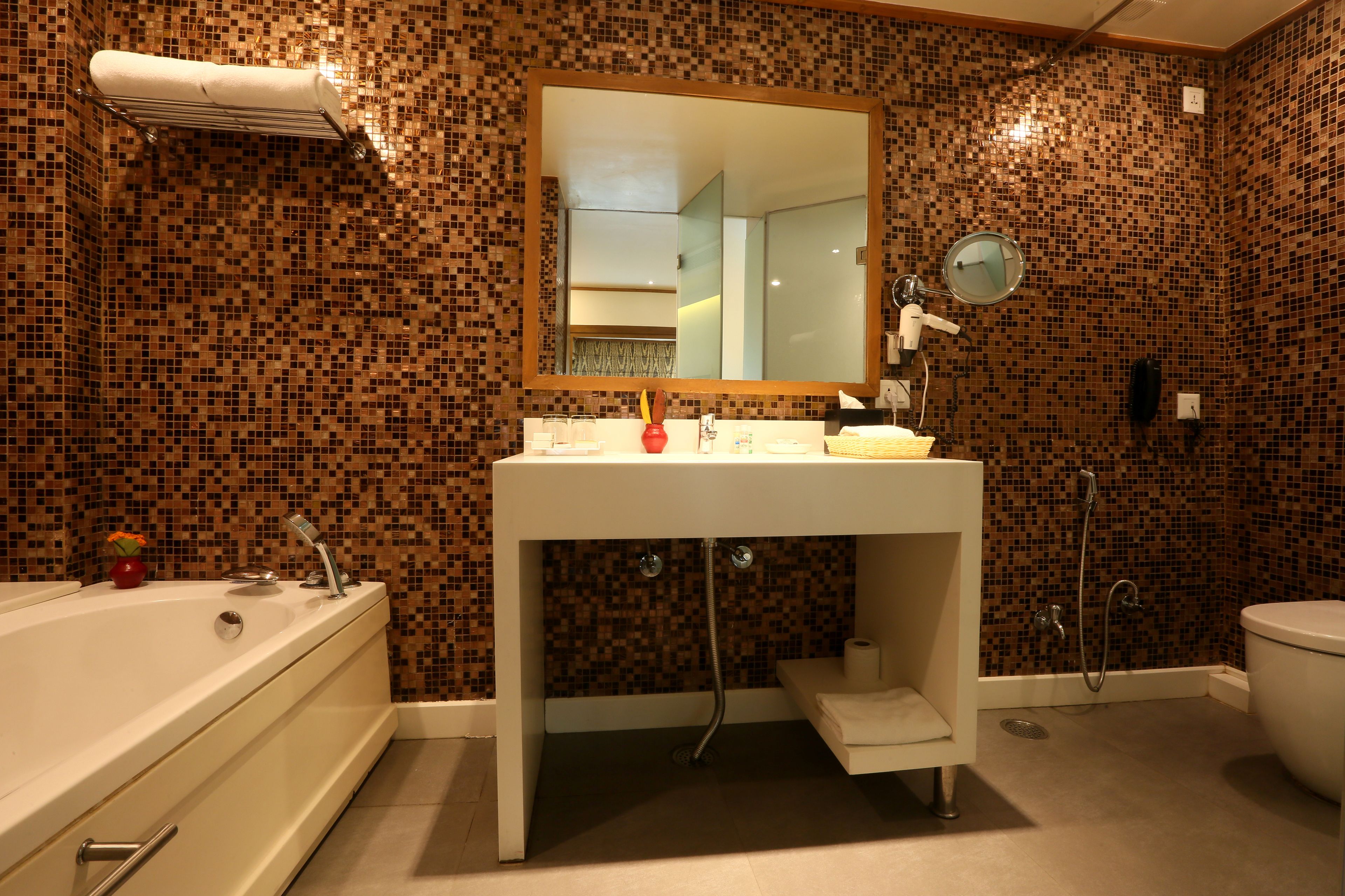 A bathroom with a mosaic tile wall, a white sink, a mirror, a bathtub, and a toilet.