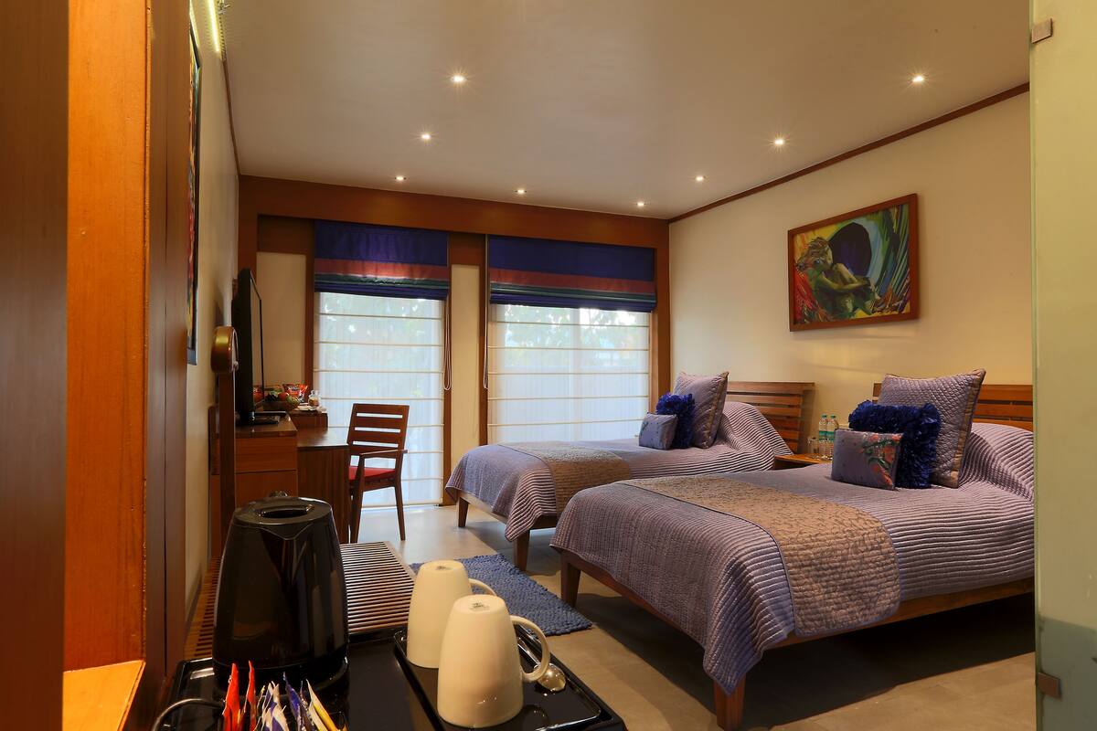 A hotel room with two beds, a desk, a chair, and a painting on the wall.