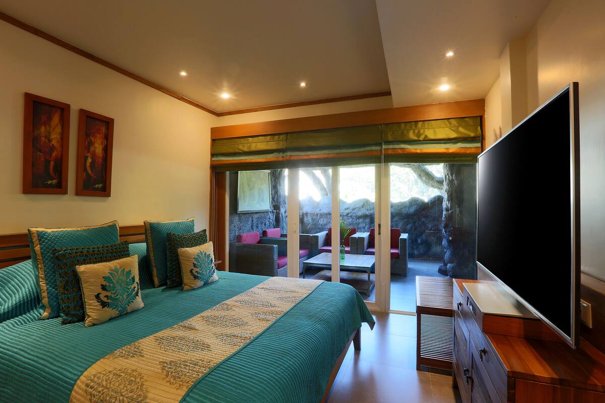 A bedroom with a large bed, a TV, and a sliding glass door leading to an outdoor seating area.