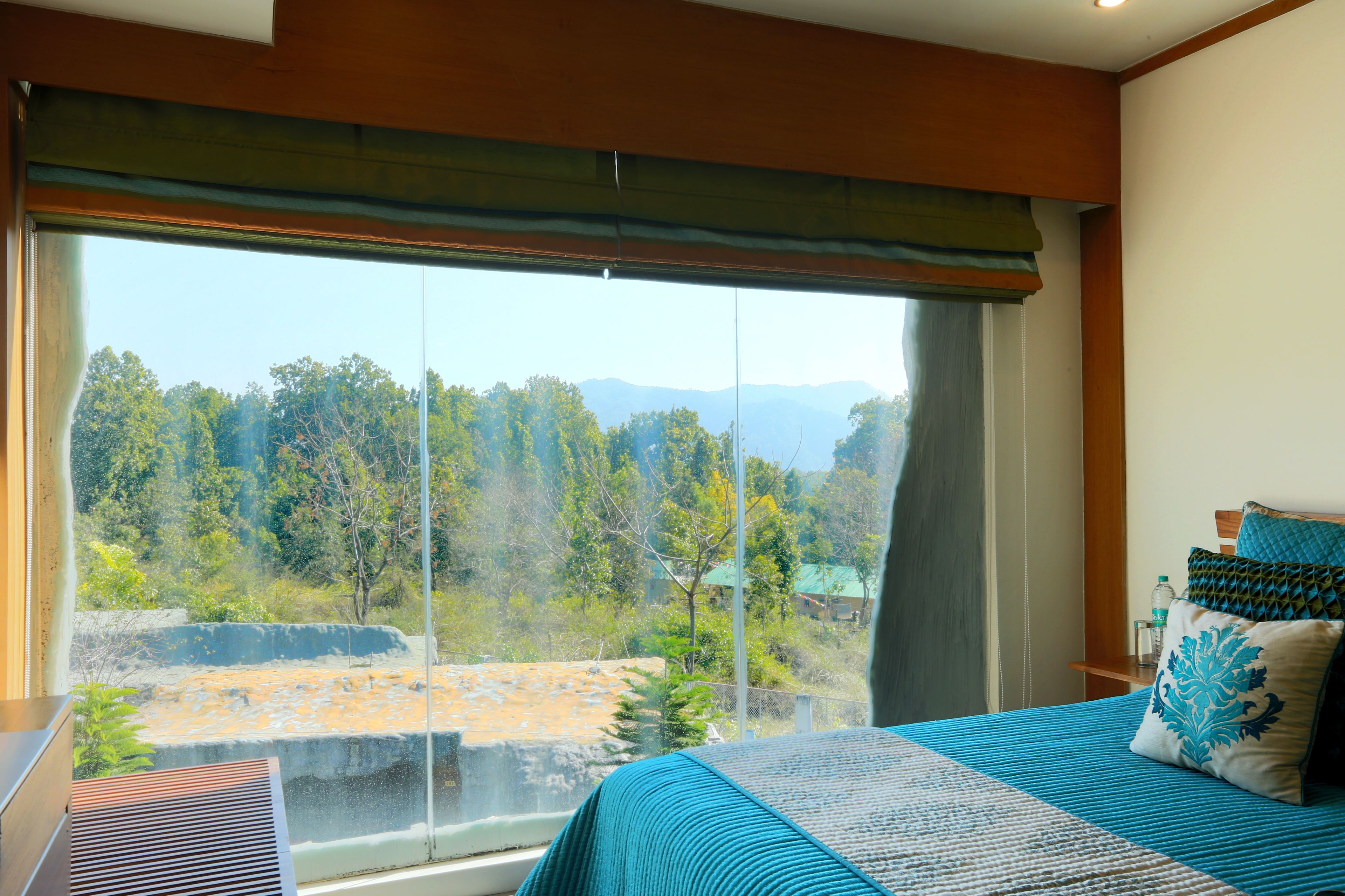 A bedroom with a large window, a bed with blue bedding, and a view of a natural landscape.