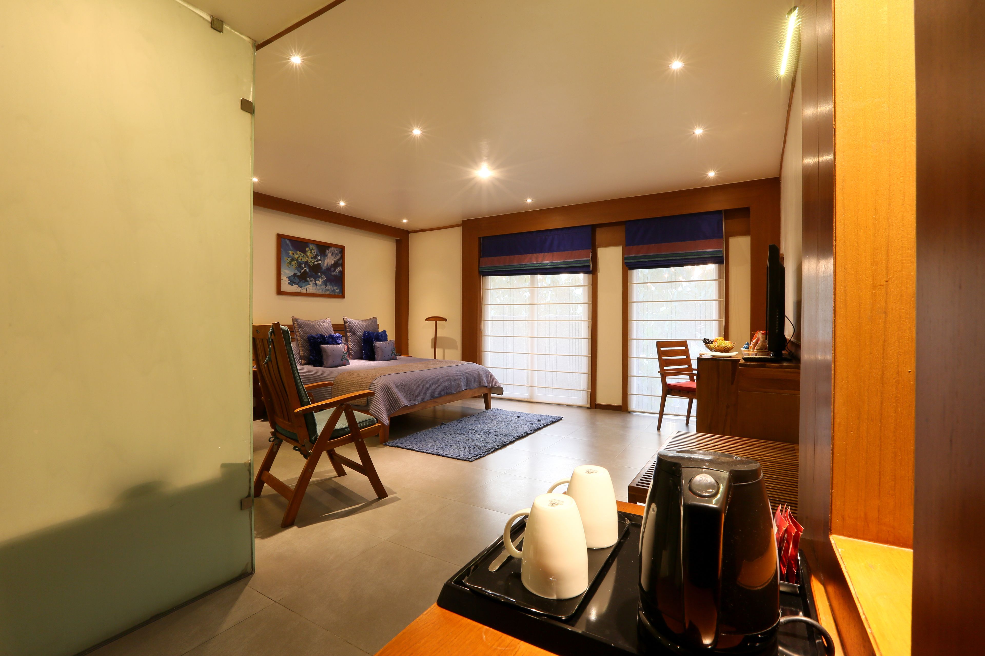 A hotel room with a bed, a desk, a chair, a coffee maker, and a window with blinds.