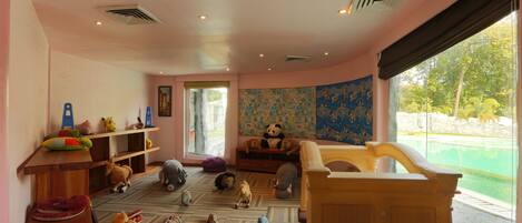 A room with a wooden crib, a large window with a view of a swimming pool, and various toys on the floor.