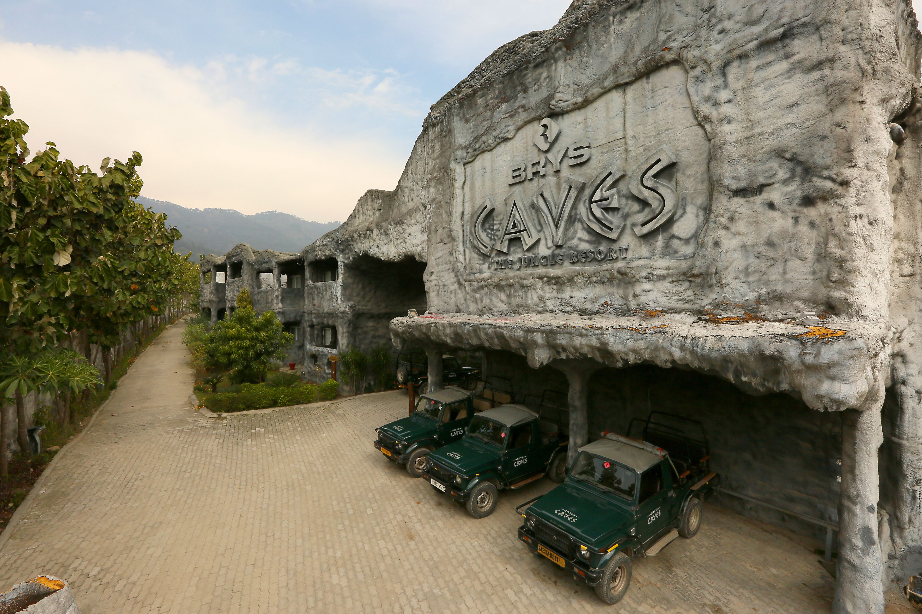 Un edificio con fachada temática de cueva y tres vehículos verdes estacionados adelante.