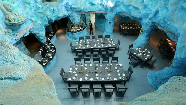 An ice-themed restaurant with tables set for dining, a central buffet, and a waiter standing. - Brys Caves (Salt)