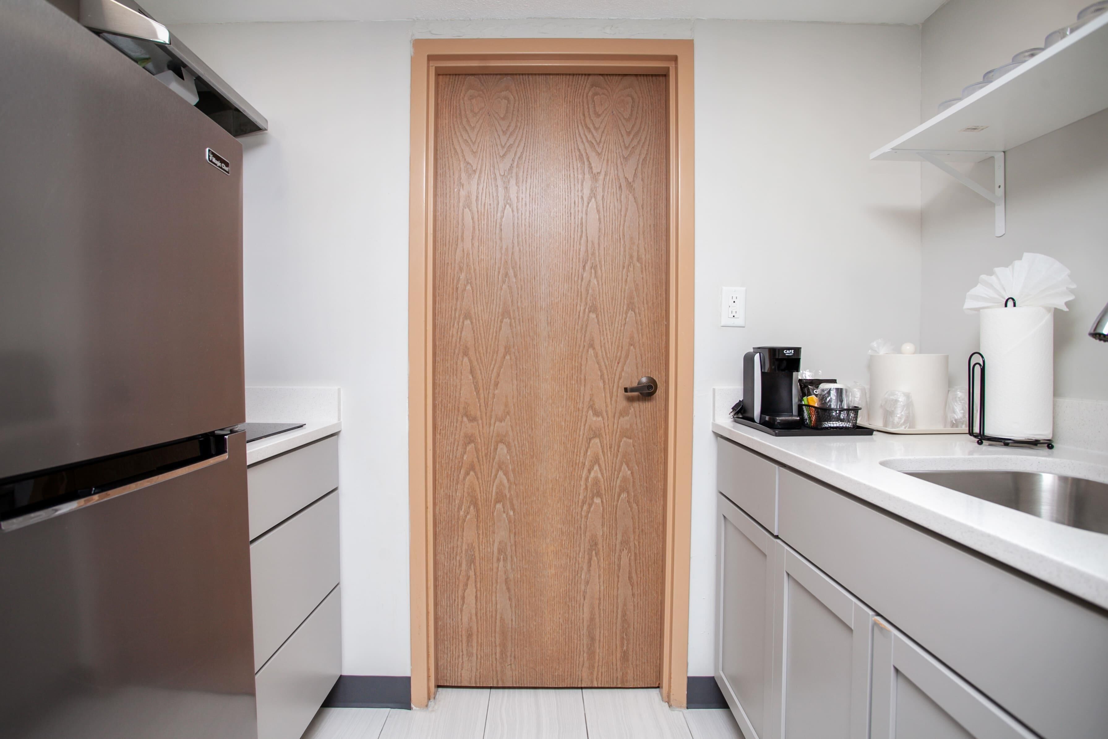 A kitchen with a wooden door, stainless steel appliances, and a white countertop.