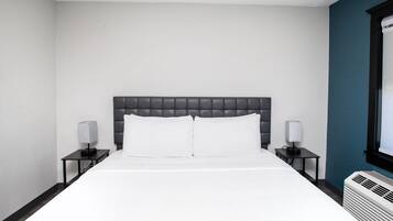 Ein Hotelzimmer mit einem Bett, zwei Nachttischen, einem Fenster und einer Klimaanlage.