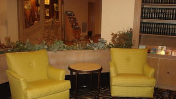 Una hall d'albergo con due poltrone gialle, un tavolino rotondo e una libreria piena di libri.