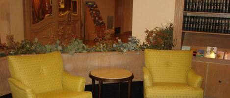 A hotel lobby with two yellow armchairs, a small round table, and a bookshelf filled with books.