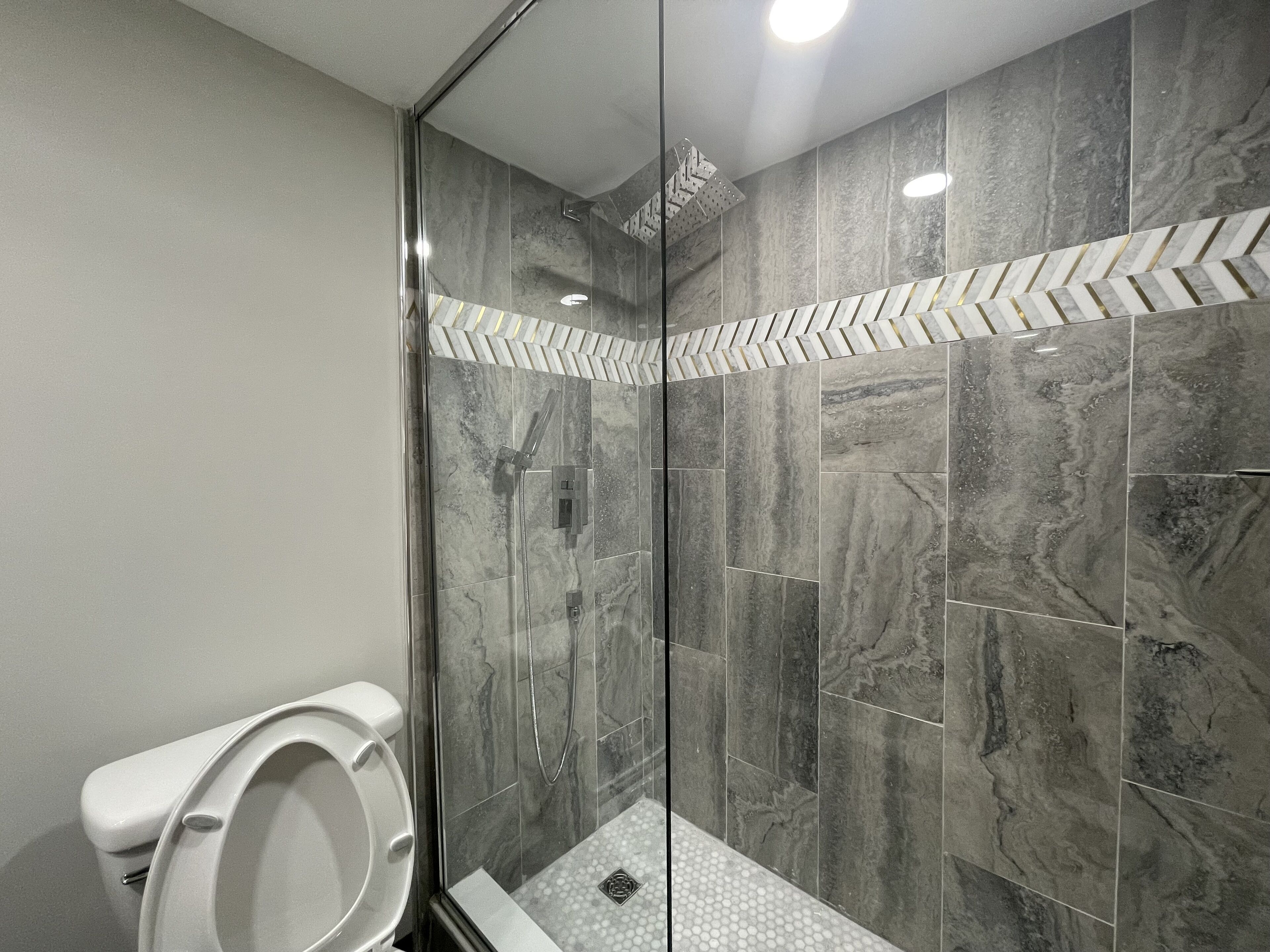 A modern bathroom with a glass-enclosed shower, marble tiles, and a white toilet.
