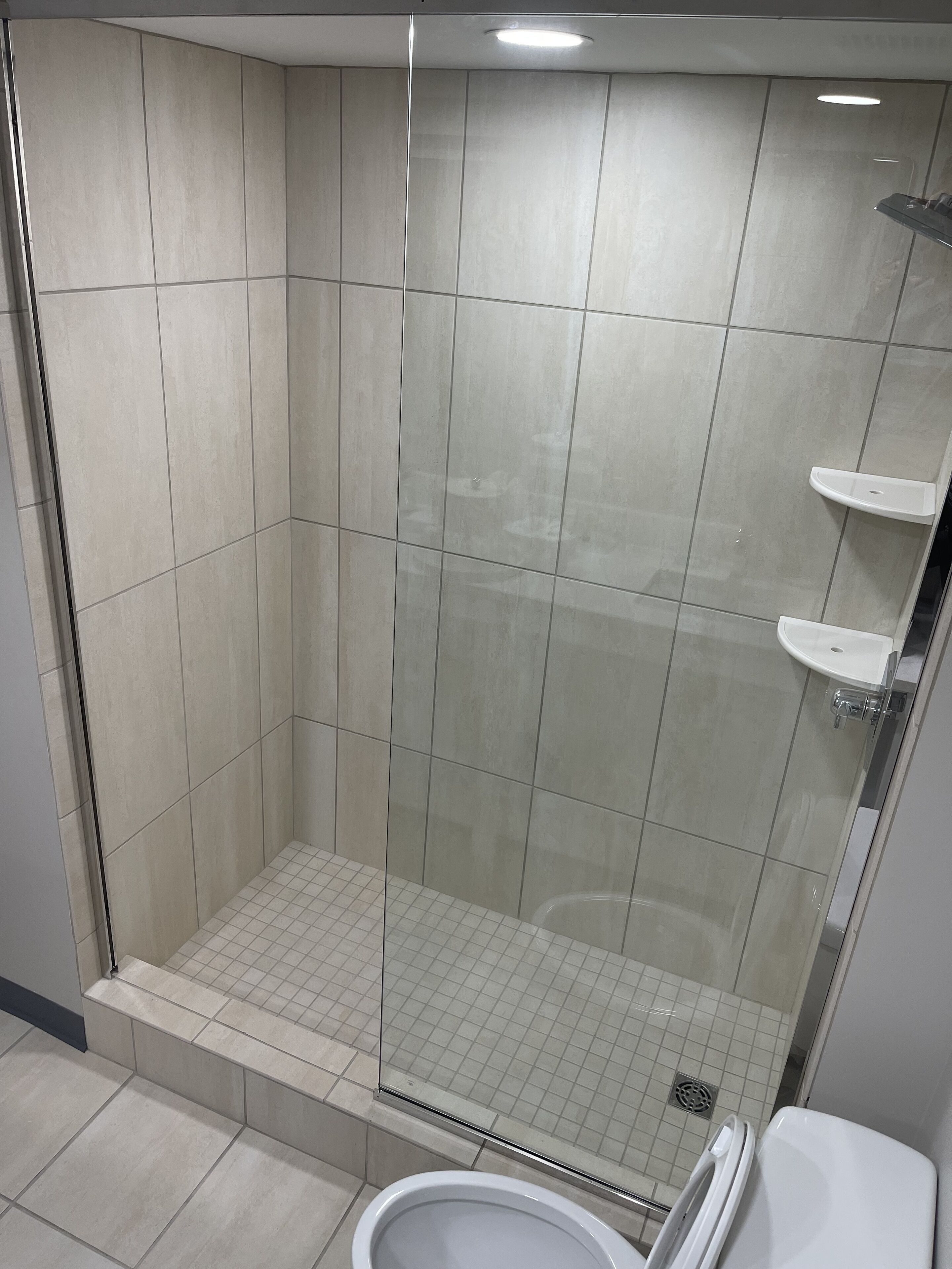 A modern shower with a glass door, a small shelf, and a tiled floor.
