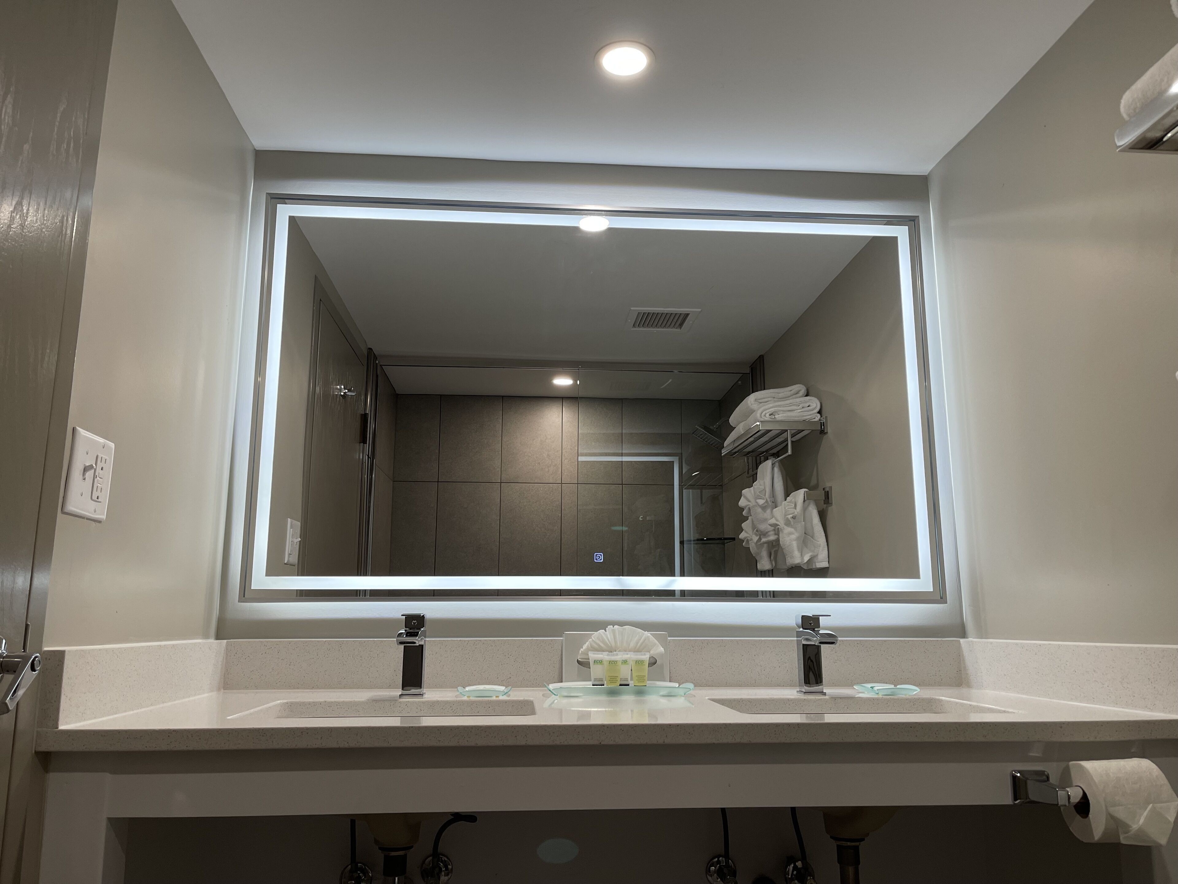 A bathroom with a large mirror, two sinks, and a towel rack.