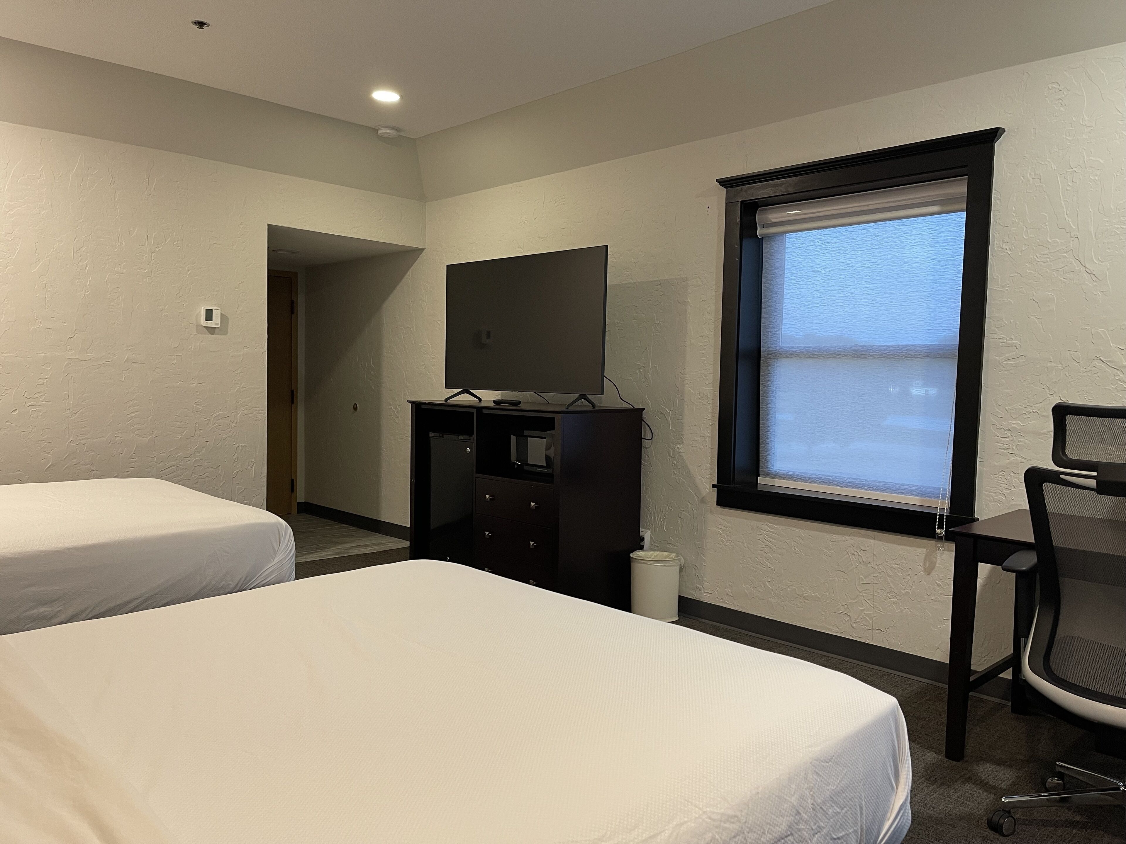 A hotel room with two beds, a desk, a chair, a TV, and a window with blinds.