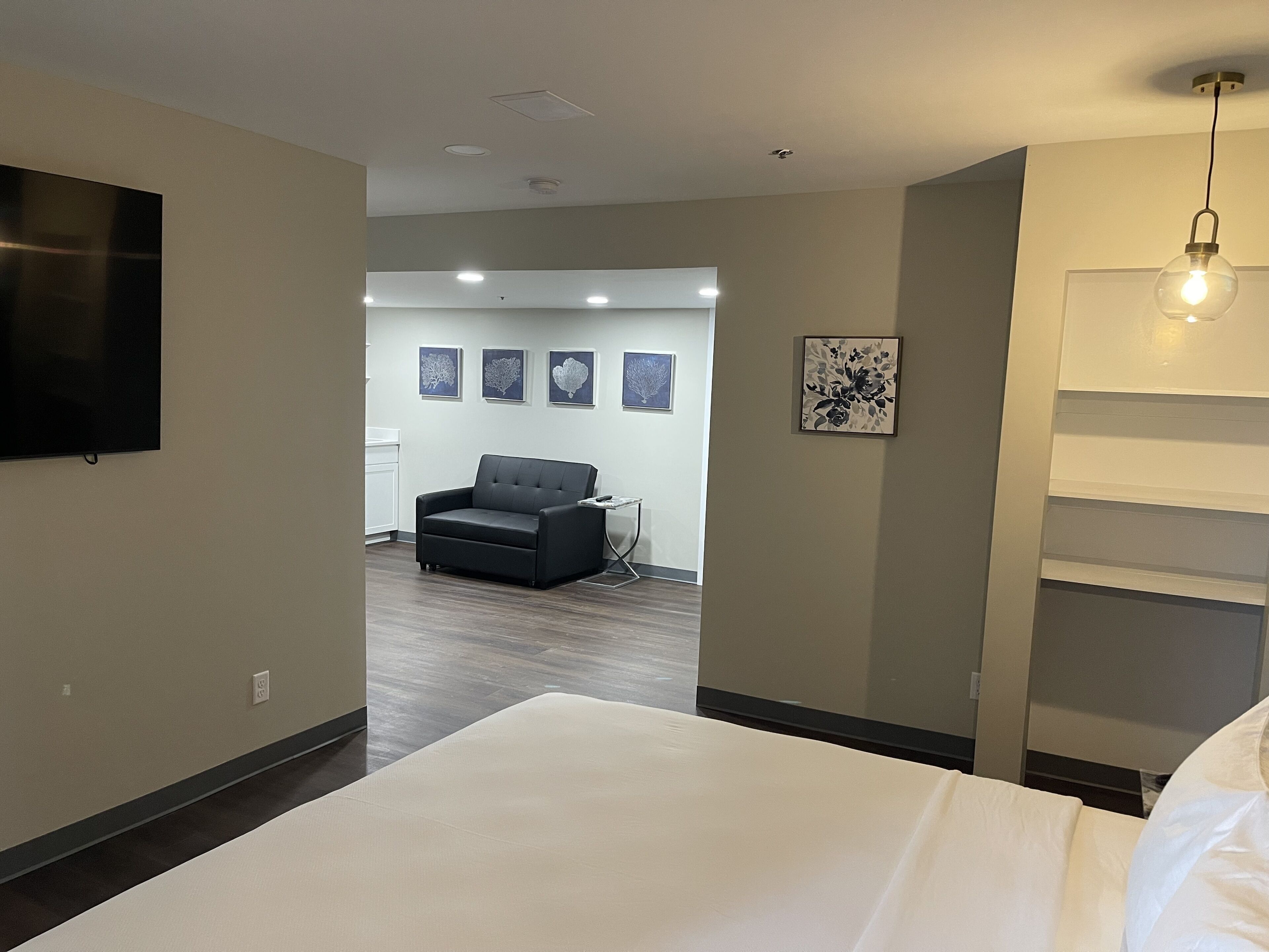 A modern hotel room with a large bed, a grey sofa, and a flat-screen TV mounted on the wall.