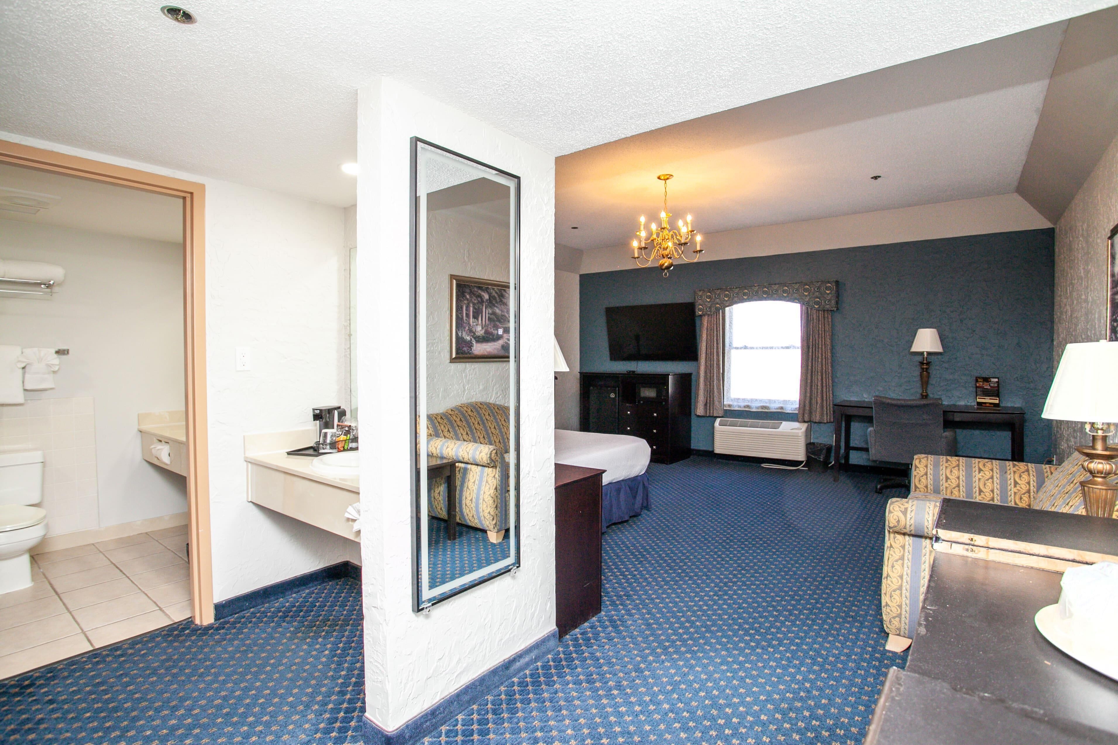 Une chambre d’hôtel comprenant un lit, un bureau, une chaise, une commode, un miroir, une télévision et une salle de bain.