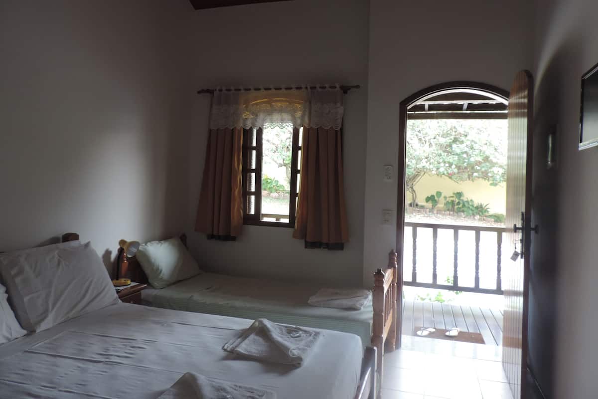 A bedroom with a bed, a nightstand, a window with curtains, and a view of the outside.