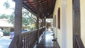 A covered wooden walkway with a railing, leading to a building with a tiled roof and a white wall. - Flats Paguru (Búzios)
