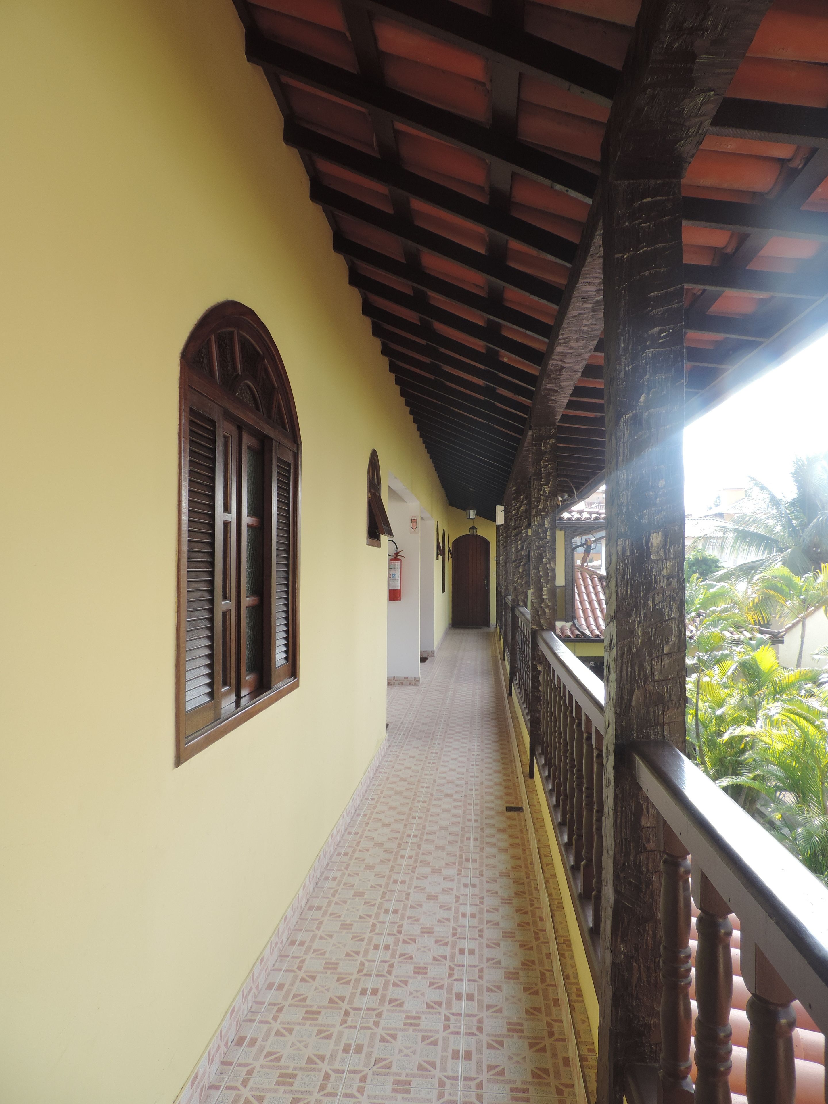 A corridor with a tiled floor, wooden window shutters, and a balcony with a railing.
