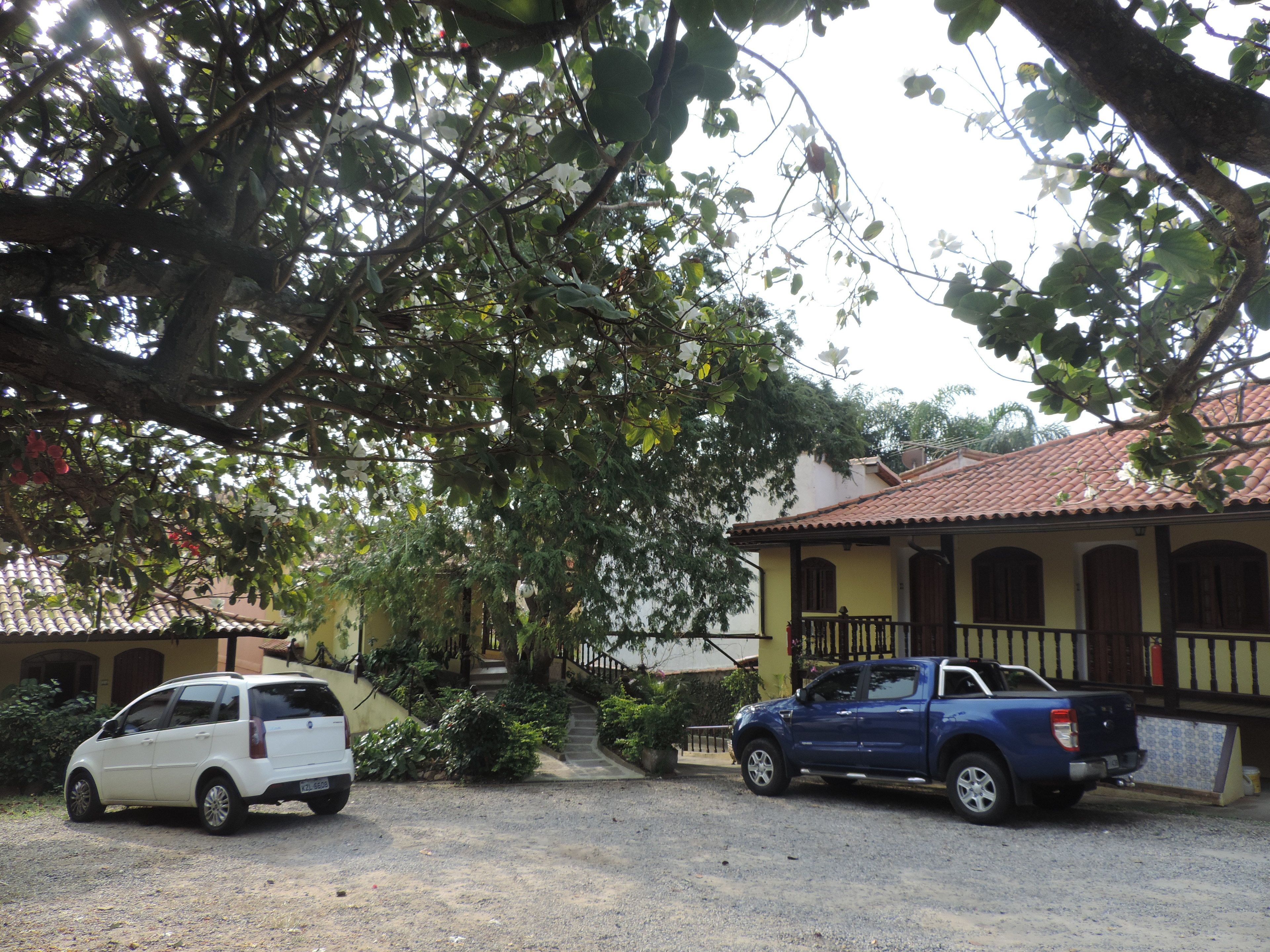 A two-story building with a tiled roof, a porch with a railing, and a driveway with two parked vehicles.