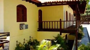 A yellow building with a wooden balcony and a small garden area. - Flats Paguru (Búzios)