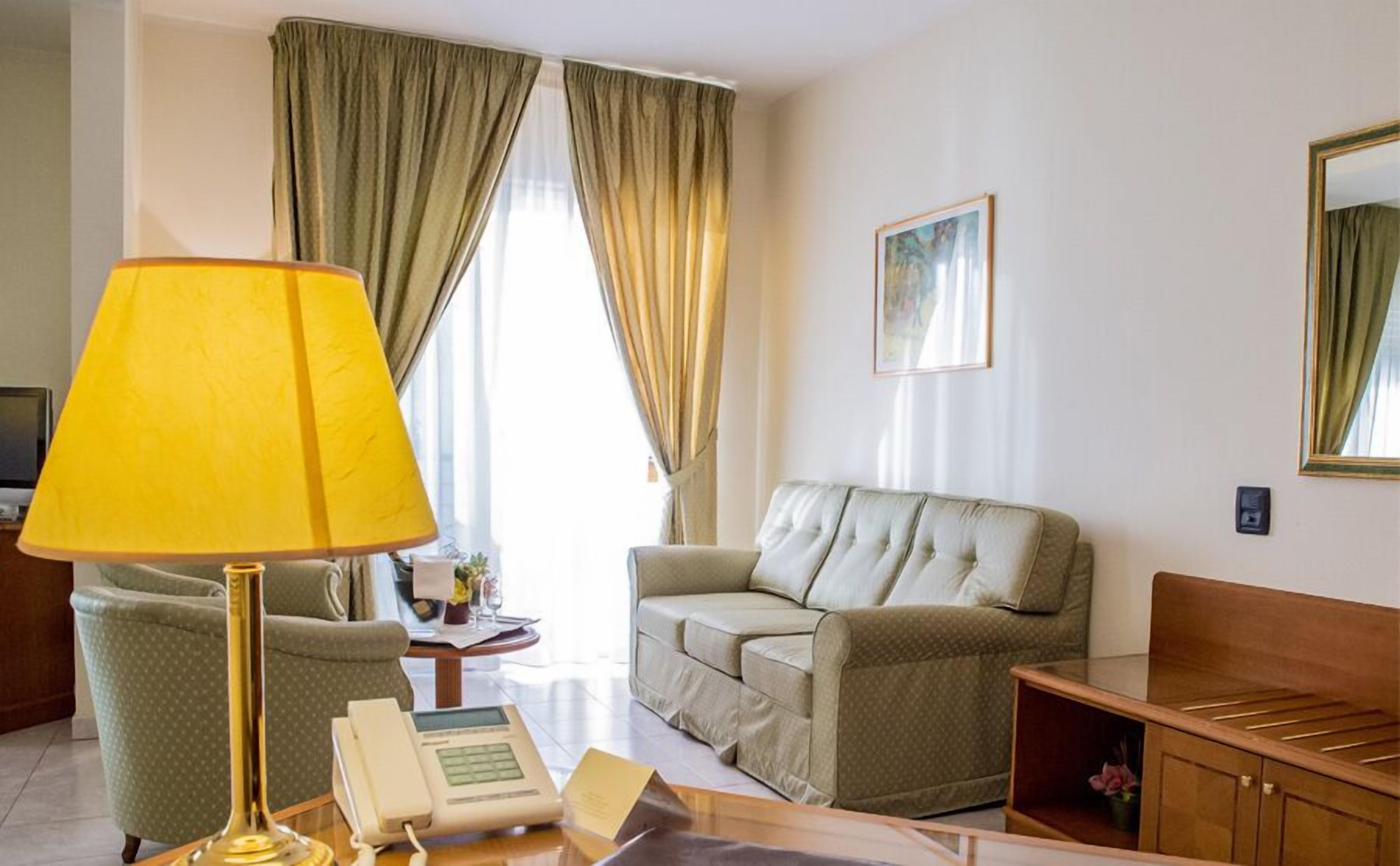 A hotel room with a sofa, a chair, a table with a telephone, and a lamp.