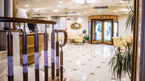 A hotel lobby with a reception desk, seating area, and a staircase.