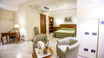 Une chambre d’hôtel comprenant un lit, deux fauteuils, une petite table avec un plateau, une bibliothèque et un bureau avec une lampe.