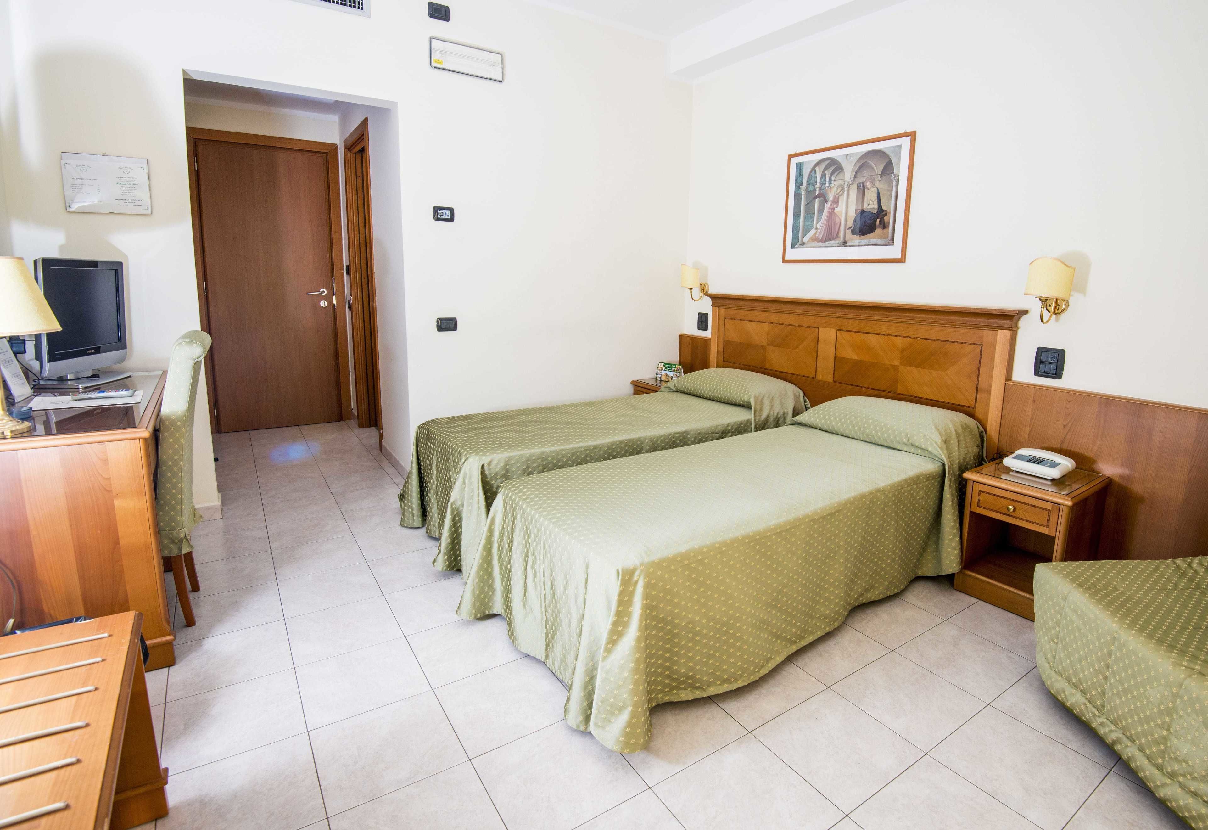 A hotel room with two single beds, a desk with a computer, a chair, and a small table.