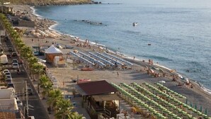 A beachside hotel with rows of umbrellas and beach chairs, a small bar, and a view of the ocean.