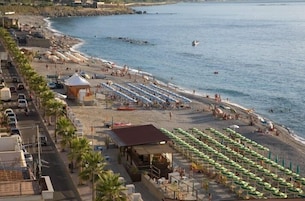 Un hotel frente a la playa con hileras de sombrillas y sillas, un pequeño bar y vistas al océano.