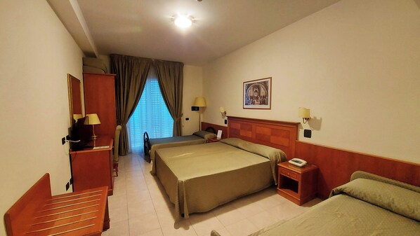 Habitación de hotel con dos camas, un escritorio, una silla, una ventana con cortinas y un cuadro en la pared.