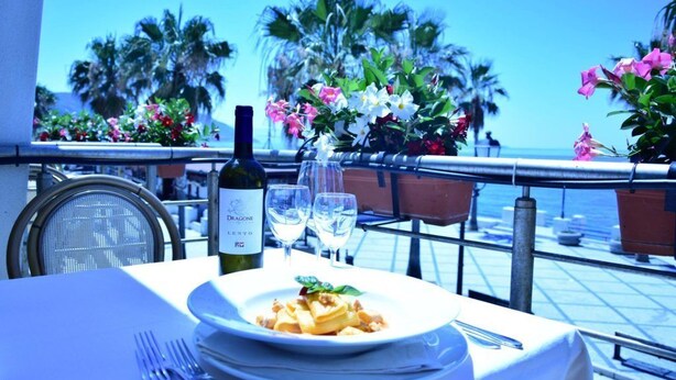 A table set for a meal with a bottle of wine, two glasses, and a plate of pasta.