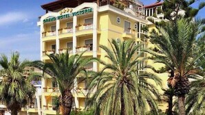 A multi-story hotel with balconies, surrounded by palm trees and a well-maintained garden.