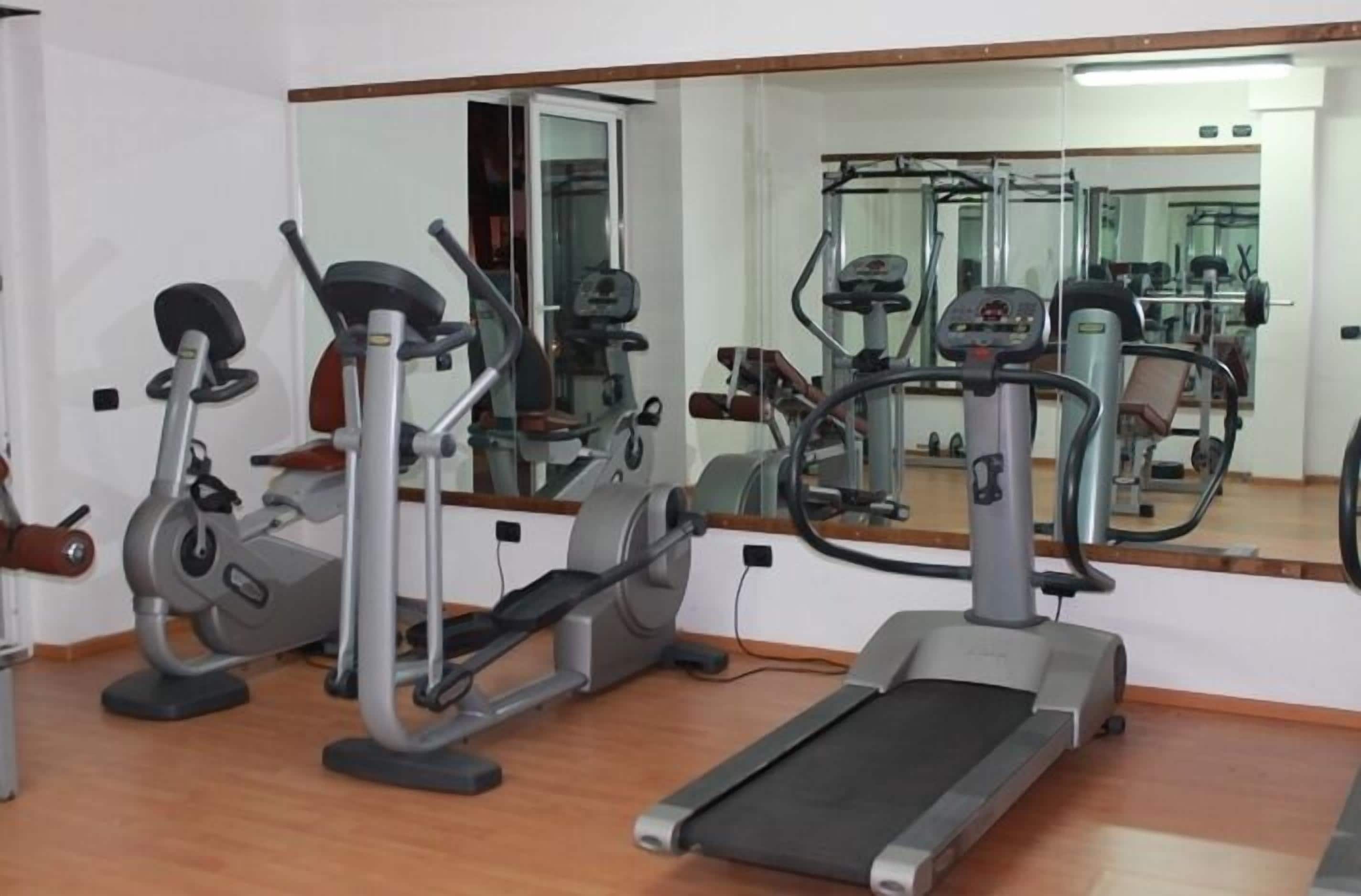 Un gimnasio con máquinas de cardio, una cinta de correr y un espejo grande.