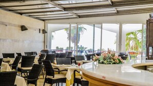 A restaurant with outdoor seating, large windows, and a view of palm trees.