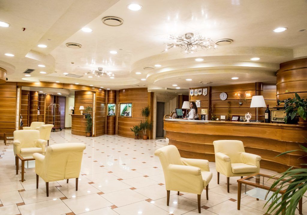 A hotel lobby with a reception desk, several chairs, and a decorative ceiling.