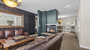 A modern lobby with a leather sofa, a chess table, a fireplace, and a large mirror.