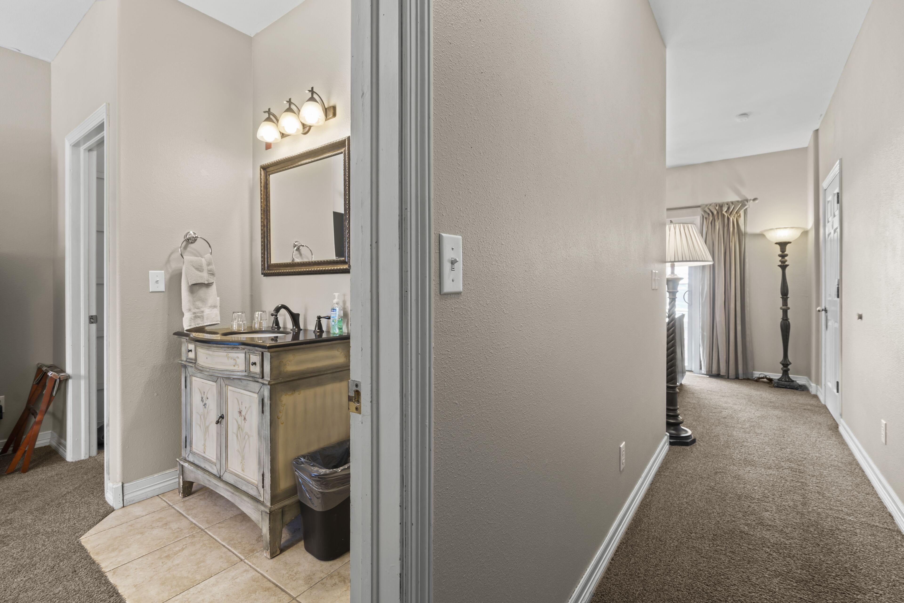 A hallway with a bathroom on the left, featuring a sink, mirror, and cabinet.