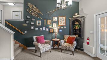 A living room with two patterned armchairs, a chandelier, a fireplace, and a collection of framed pictures on the wall.