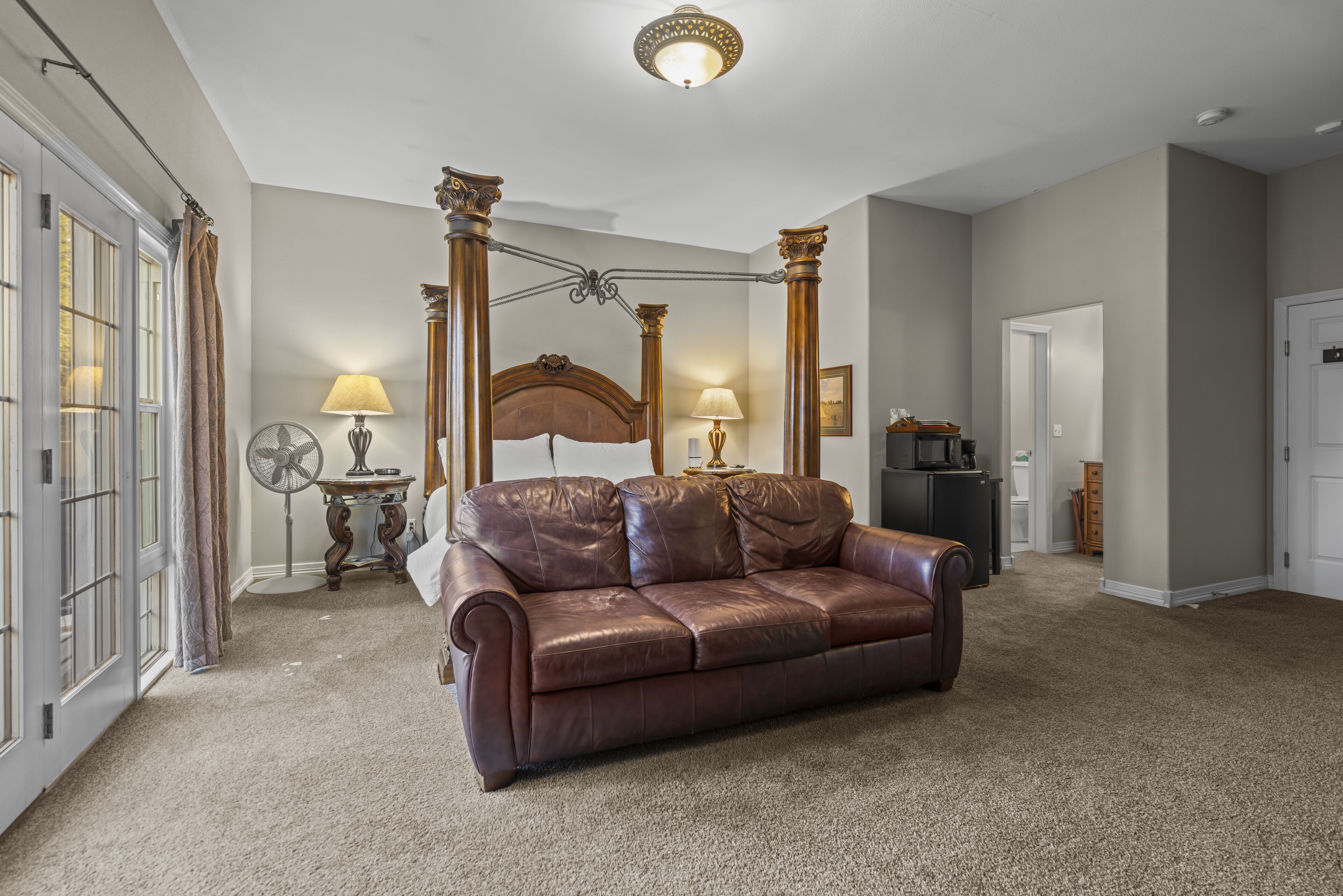 A spacious room with a brown leather sofa, a four-poster bed, and a fan.
